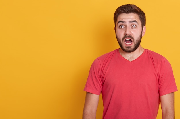 Horizontal portrait of astonished brunet man, wearing red casual shirt, poses against yellow