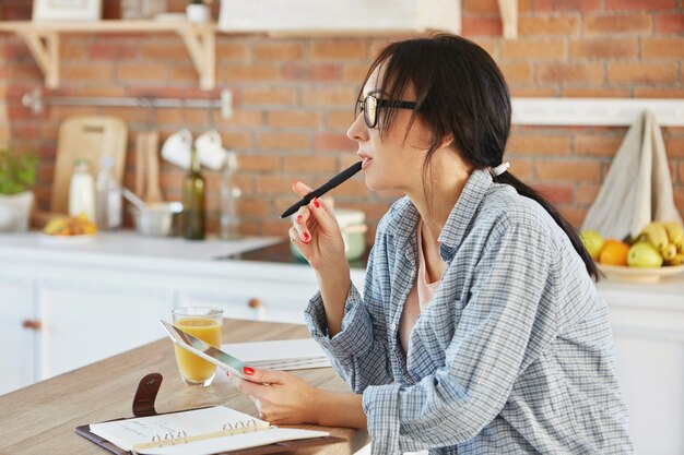 Horizontal portrait of brunette female wears loose casual shirt, looks pensively aside