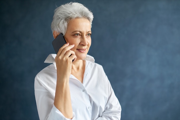 携帯電話を保持している白いシャツで忙しい中年白人女性マネージャーの横向きの肖像画