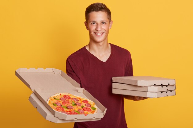 Горизонтальный портрет веселый харизматичный курьер смотрит прямо, держа открытую коробку пиццы