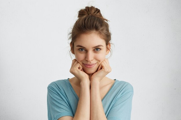 Horizontal portrait of cute young woman with blue eyes and gentle smile holding hands under chin looking contented and carefree.