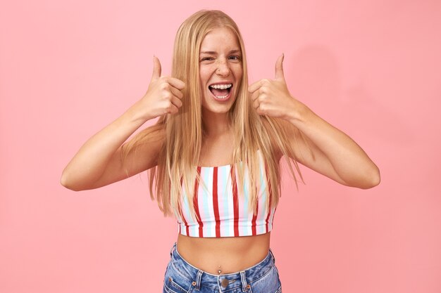 Horizontal Portrait of emotional overjoyed young European female wearing summer clothes, piercing on nose and belly button, enjoying nice cool party