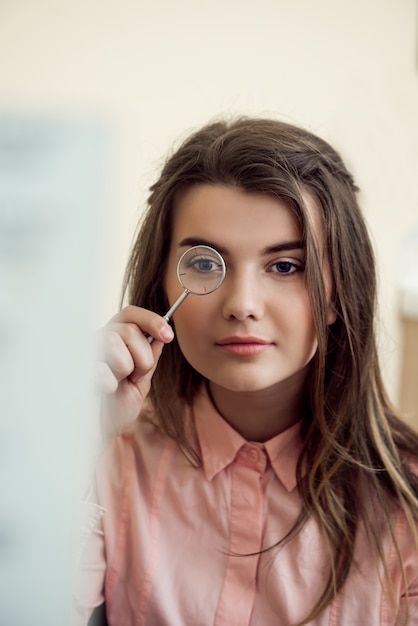 眼科医がレンズを持ち、ワードチャートを読んで視力を確認しようとする際にそれを覗き込むことで、面倒見の良い集中型女性の水平方向の肖像画。アイケアと健康の概念