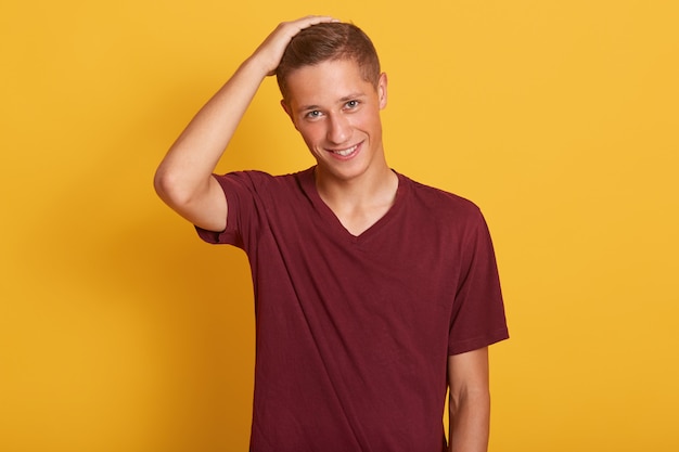 Horizontal portrait of handsome male adult keeping hand on his head, analyzing information or makes decision