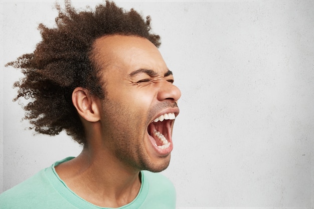 Free photo horizontal portrait of man with dark skin and afro hairstyle screams in despair, opens mouth widely, being in panic