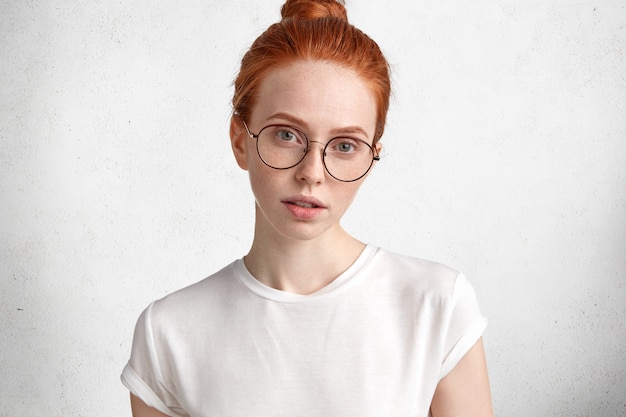 Горизонтальный портрет серьезной рыжеволосой девушки в больших круглых очках загадочным выражением смотрит прямо в камеру