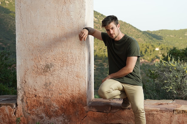 Horizontal shot of an attractive young male leaning on his leg and posing next to an old wall