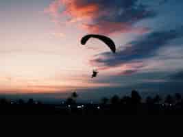 Foto gratuita inquadratura orizzontale di una spiaggia con una persona che scivola su un paracadute paramotore