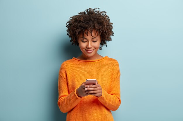 スマートフォンデバイスに焦点を当て、友人とオンラインチャットする美しい満足している女性のティーンエイジャーの水平方向のショット