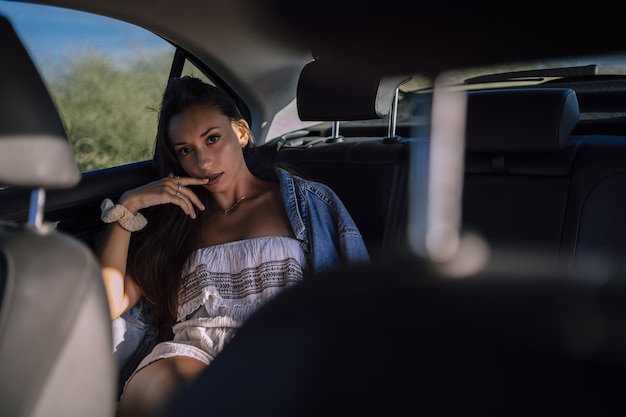 Горизонтальный снимок красивой молодой кавказской девушки, позирующей на заднем сиденье автомобиля в поле