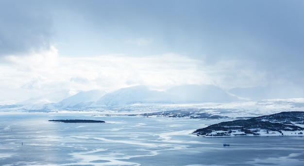 Horizontal shot of a body of water covered with ice surrounded by mountains under the white clouds
