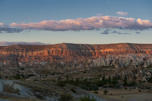 Горизонтальный снимок каньона с несколькими растениями у его подножия и облаками в небе