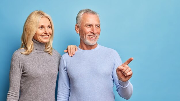 Horizontal shot of cheerful middle aged woman and man smiles gladfully and look into distance.