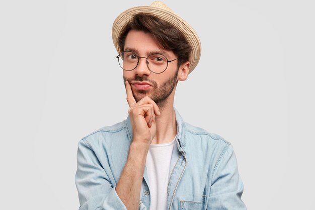 Horizontal shot of confident bearded male keeps finger on chin