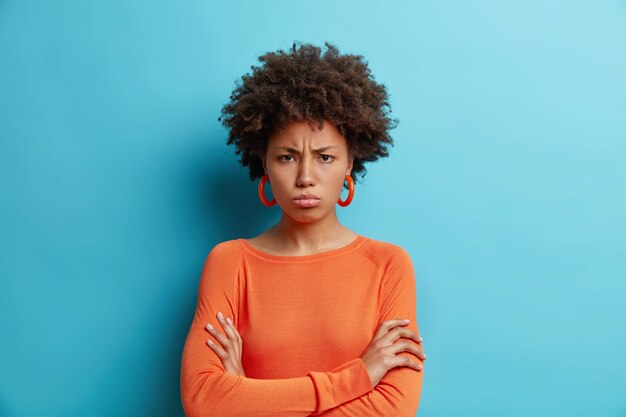 Horizontal shot of dark skinned offended woman with Afro hair keeps arms folded has offensive expression