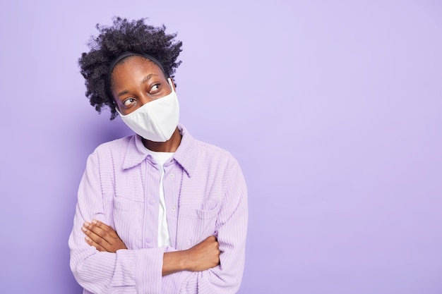 Horizontal shot of dark skinned thoughtful woman wears disposable mask as coronavirus protection