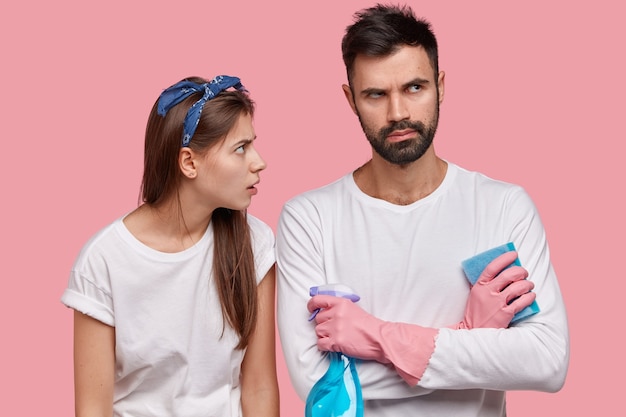 Horizontal shot of displeased young European female maid looks with tired expression at partner who feels annoyed, keeps arms folded