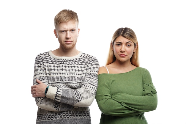 Horizontal shot of distrustful young couple crossing arms and staring, having doubtful skeptical looks. Human facial expressions, emotions, feelings, attitude and body language