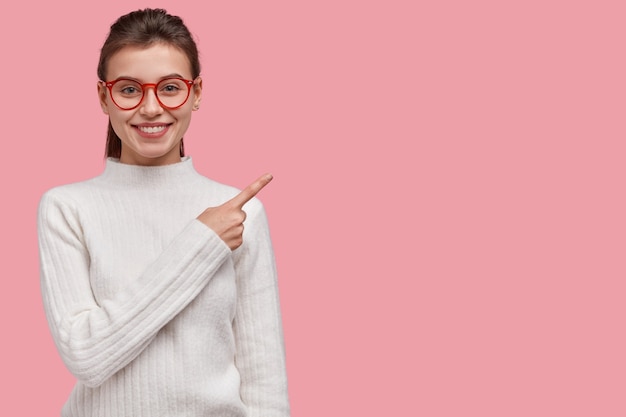 Free photo horizontal shot of european woman with dark hair, points with fore finger at upper right corner