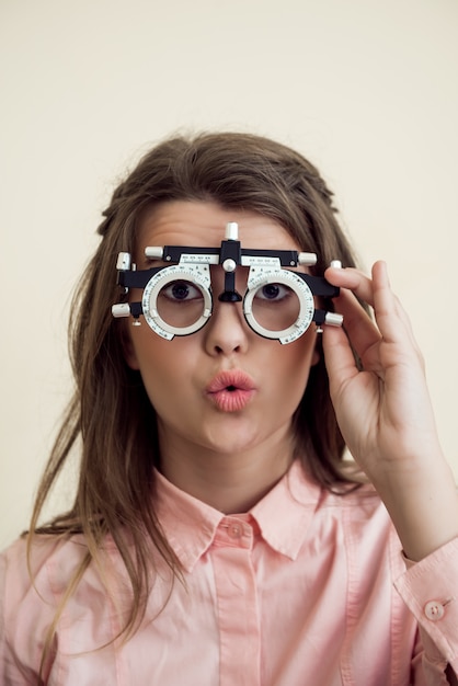 Horizontal shot of excited cute european brunette checking vision with phoropter, being interested in how it works, waiting for optometrist to prescribe appropriate glasses