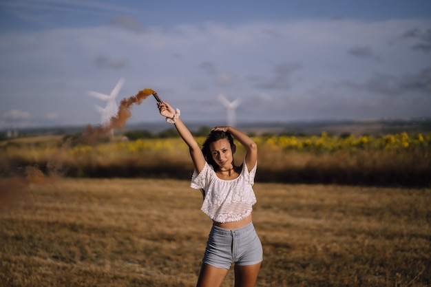 Horizontal shot of a female posing with a smoke bomb on a background of fields and windmills