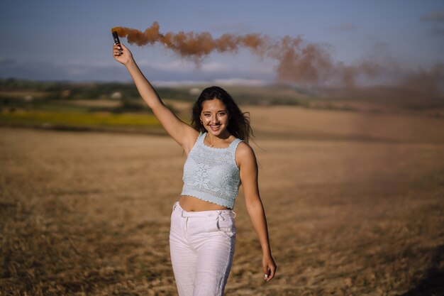 Horizontal shot of a female posing with a smoke bomb on a background of fields and windmills