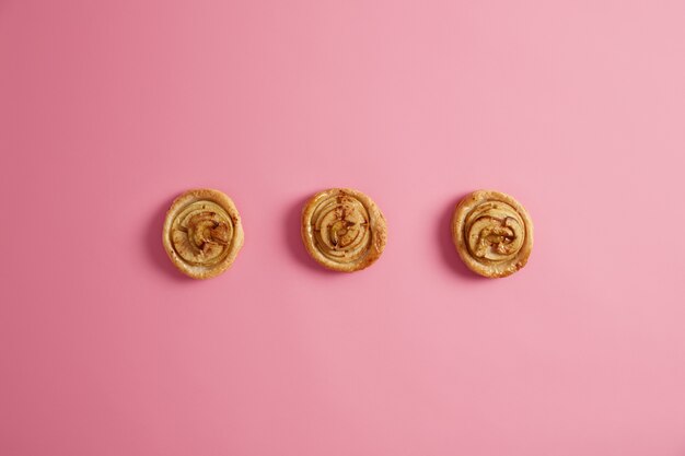 Horizontal shot of fresh homemade swirl cinnamon buns isolated on pink  background. Sweet tooth, temptation and junk food concept. Yummy dessert. Breaking diet. Delicious sugary rolls.