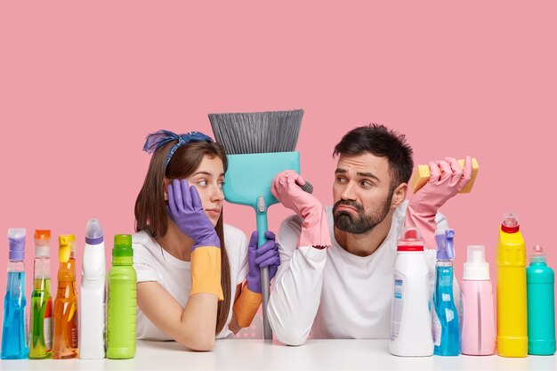 Горизонтальный снимок разочарованных занятых женщин и мужчин, которые перегружены работой и испытывают стресс, несут кисть, используют необходимые принадлежности для уборки