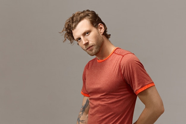 Horizontal shot of handsome bearded European guy with fit athletic body going to have running exercise, posing isolated at blank wall with copyspace for your promotional information