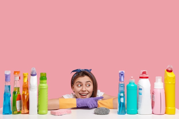 Horizontal shot of happy Caucasian woman with toothy smile, wears rubber protective gloves