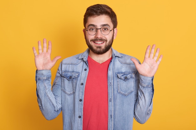 Horizontal shot of happy joyful funny guy having beard, raising arms, making gesture, 