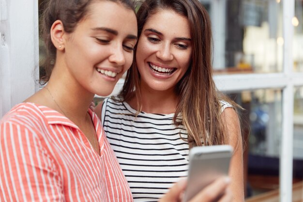 Horizontal shot of happy young girlfriends watch smartphone screen