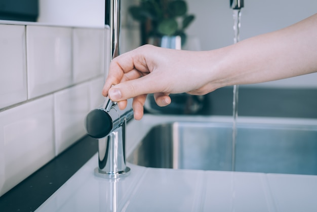 Horizontal shot of a human hand opening the modern sink for the flow of water