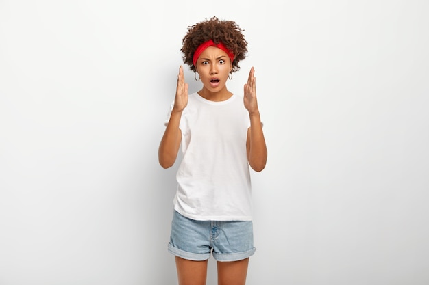 Horizontal shot of impressed curly ethnic woman measures with two hands, shows big and large sign