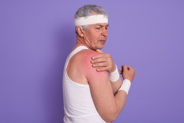 Horizontal shot of injured senior man posing sideways, mature male with white head band, elderly sportrsman