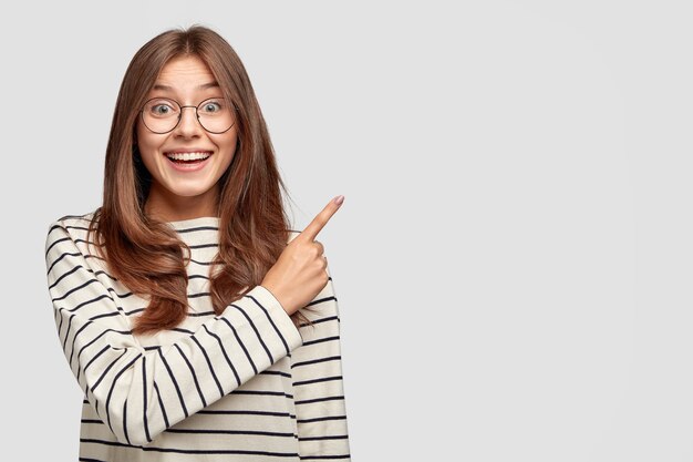 Horizontal shot of joyful young woman with glasses posing against the white wall