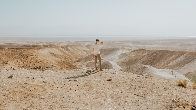 Horizontal shot of a male with a white shirt standing on the edge of a mountain enjoying the view