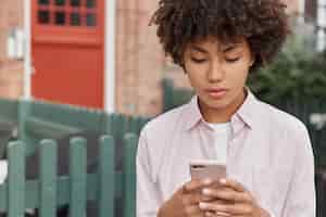 無料写真 巻き毛の髪型、屋外散歩、携帯電話を保持している深刻な黒人の10代の少女の水平方向のショット