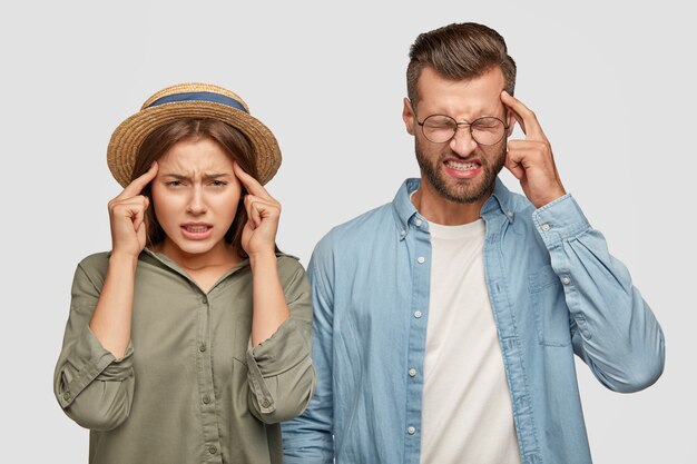 Horizontal shot of overworked tired coworkers keep index fingers on temples, suffer from headache