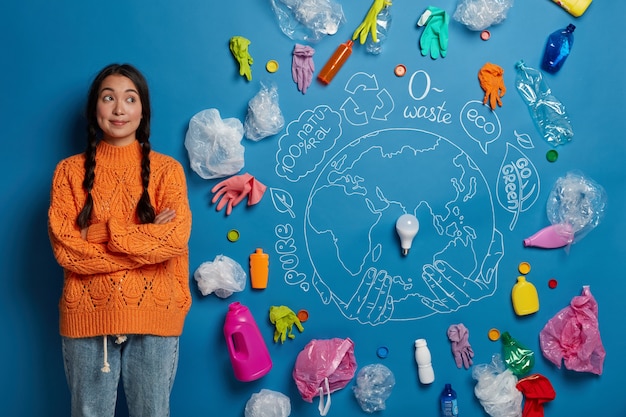 Foto gratuita inquadratura orizzontale della donna asiatica pensierosa tiene le mani incrociate, raccoglie la spazzatura e pensa ai problemi di ecologia