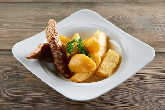 Horizontal shot of a plate with fried potatoe slices and chicken sausage on a wooden table dinner meal lunch supper meat eating hungry delicious vegetable grilled roasted