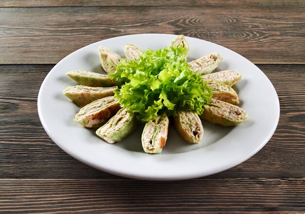 Horizontal shot of a plate with pancake rolls with creamy filling decorated with salad on a wooden table restaurant cafe grocery traditional recipe ingredients delicious concept.