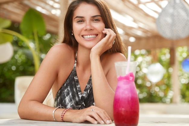 Il colpo orizzontale della donna adorabile felice ha un sorriso piacevole trascorre il tempo di ricreazione si siede in un caffè all'aperto, incontra un amico.