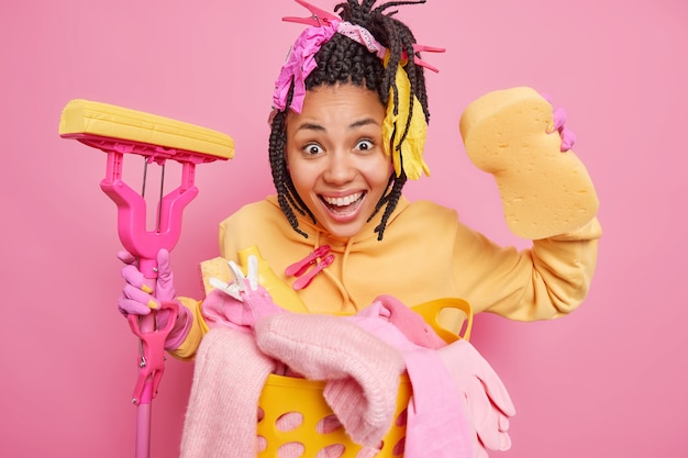 Horizontal shot of positive dark skinned housewife with braids holds mop