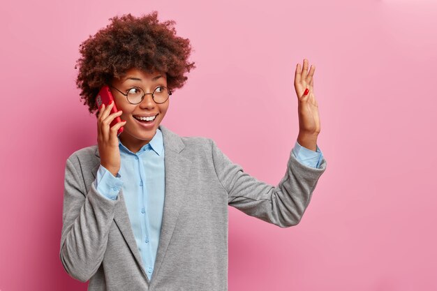 Free photo horizontal shot of positive dark skinned woman with curly hair waves palm aside