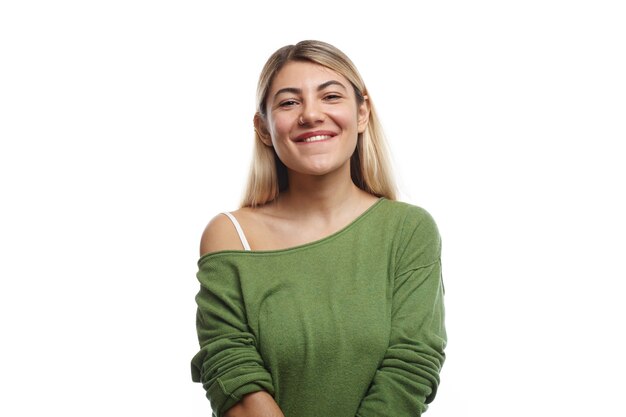 Горизонтальный снимок позитивной молодой европейской студентки с кольцом в носу и крашеными волосами, которая позирует со счастливой очаровательной улыбкой и чувствует себя расслабленной после лекций в университете