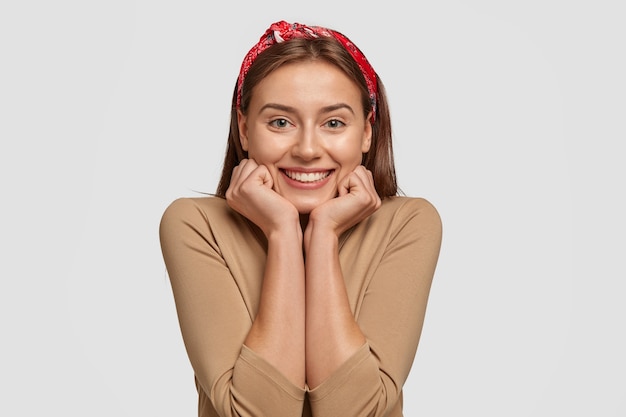 Horizontal shot of pretty Caucasian woman holds chin with both hands