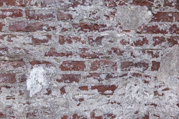 Horizontal shot of a red and white old stone wall with texture and some plaster on it
