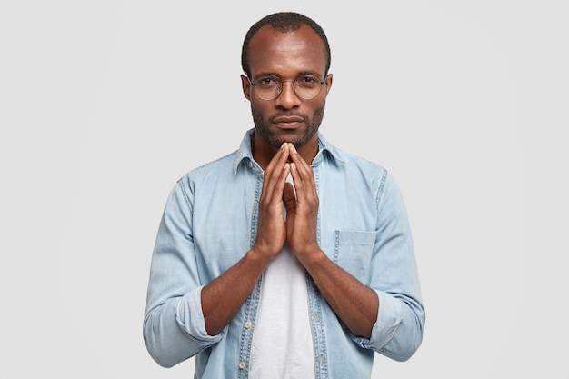 Horizontal shot of serious dark skinned boyfriend keeps hands together, asks for forgiveness