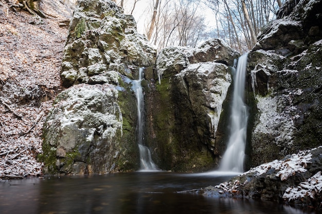 Horizontal shot of several waterfalls coming out of huge snowy rocks in the winter season
